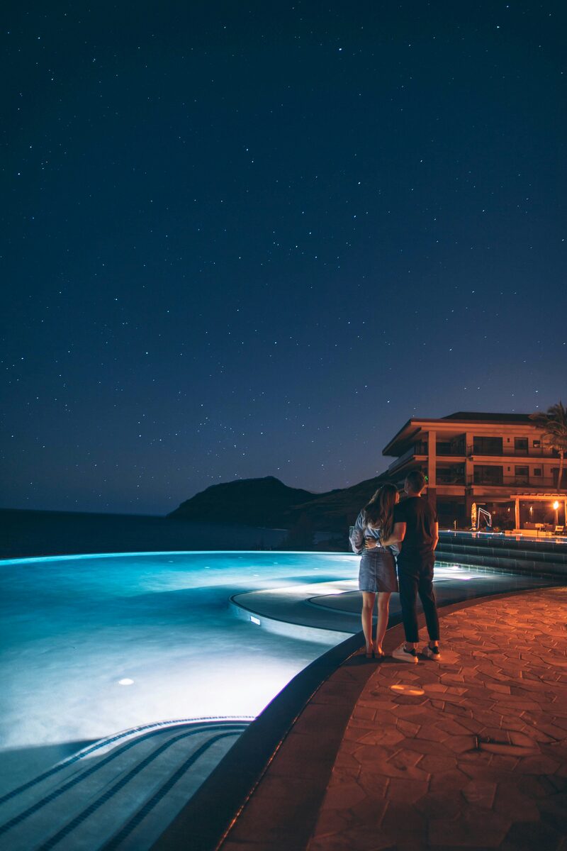 Couple standing by an infinity pool under a starry night sky